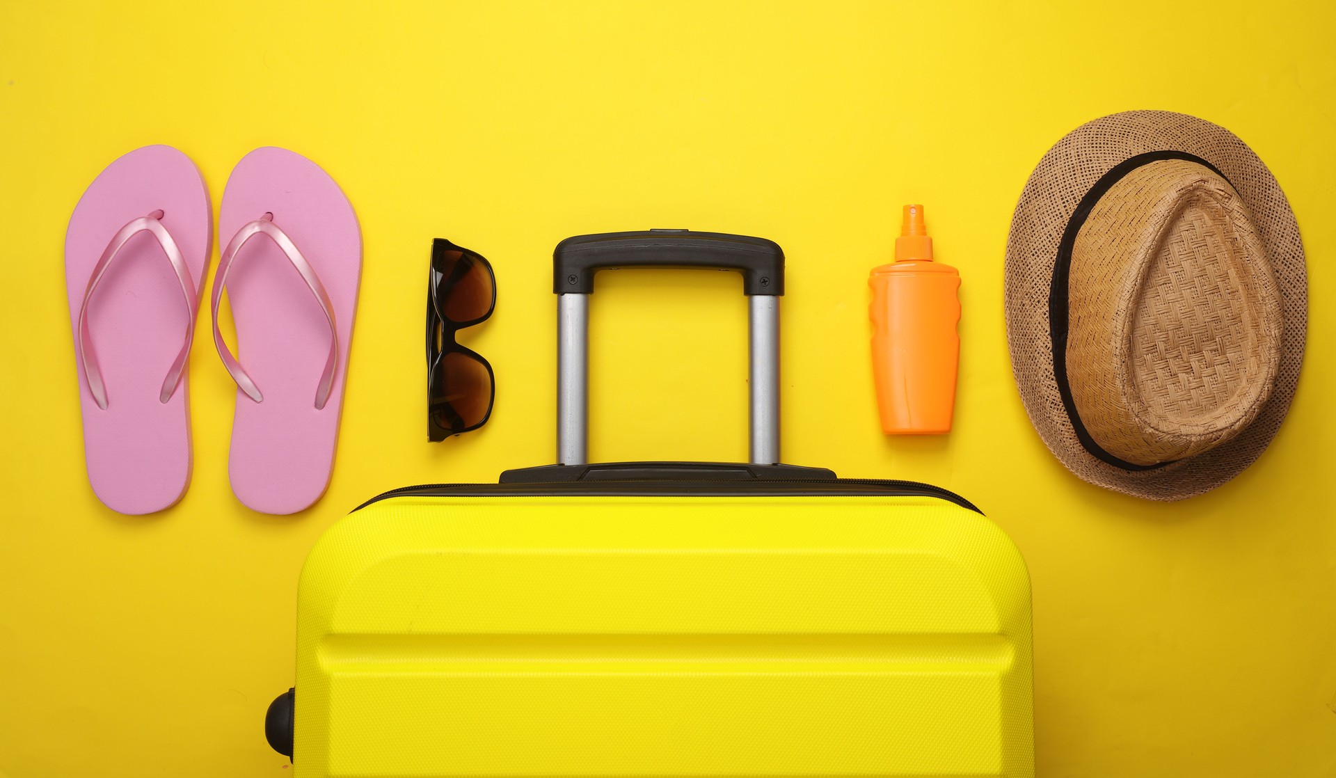 Beach vacation, summer holiday, relocation concept. Suitcase luggage with beach accessories on yellow background. Top view. Flat lay